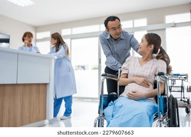 Asian husband taking care of pregnant woman sitting on wheelchair. Attractive couple, male and enceinte female smiling look at each other after receive treatment from doctor in medical hospital ward. - Powered by Shutterstock