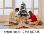 Asian husband and wife couple lover decorating Christmas tree together while the man helping woman packing decoration boxes.