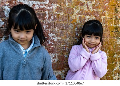 Asian Identical Female Twins Child Wearing Jacket During Cold Weather And Standing On An Old Brick Wall Background