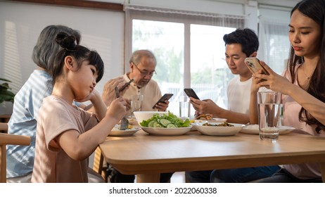 Asian Ignoring Family Not Paying Attention On Small Child While Eating. Upset Daughter Sitting At Lunch Table Looking To Addicted Parents And Grandparents Using Smartphones. Bad Parenting In House.