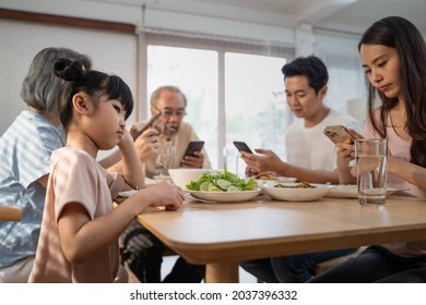 Asian Ignoring Family Not Paying Attention On Small Child While Eating. Upset Daughter Sitting At Lunch Table Looking To Addicted Parents And Grandparents Using Smartphones. Bad Parenting In House.