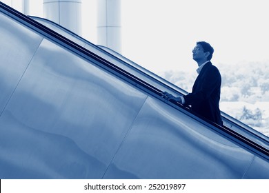 Asian Indian Businessman Going Up Escalator, Side View In Blue Tone.