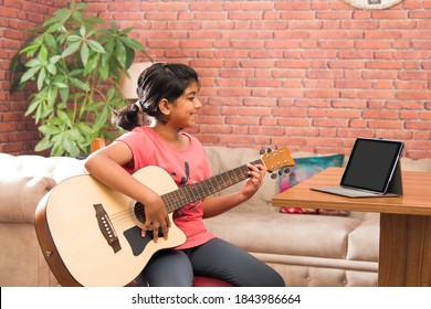 Asian Indian child learning music or musical instrument online using laptop computer or tablet at home, persuing hobby
