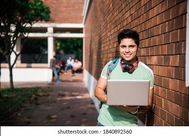 Asian Indian College Student In Focus Working On Laptop Or Reading Book While Other Classmates In The Background, Outdoor Picture In University Campus