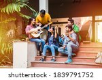 Asian Indian college students playing music with guitar while sitting in campus on stairs or over lawn