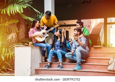 Asian Indian college students playing music with guitar while sitting in campus on stairs or over lawn - Powered by Shutterstock