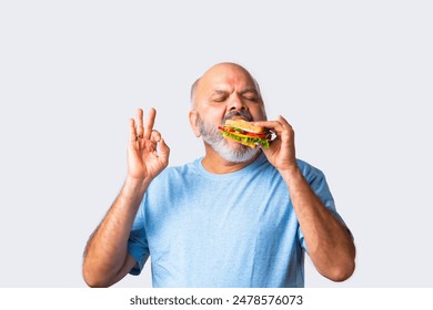 Asian Indian elderly old senior man eating tasty vegetable sandwich, isolated - Powered by Shutterstock