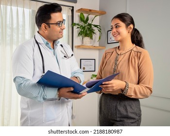 Asian Indian man or male physician or doctor wearing stethoscope and apron holding report file in hand and giving consultation to a smiling female or happy Woman patient. Medical, medicine, healthcare - Powered by Shutterstock