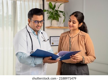 Asian Indian man or male physician or doctor wearing stethoscope and apron holding report file in hand and giving consultation to a smiling female or happy Woman patient. Medical, medicine, healthcare - Powered by Shutterstock