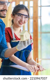 Asian Indian Professional Male And Female Engineer Architect Foreman Labor Worker Lover Couple Wear Safety Goggles Standing Cuddling Leaning Together Holding Wooden Home Model In Construction Site.