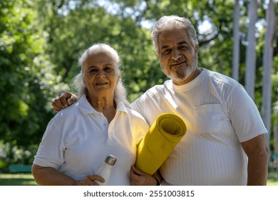 Asian or Indian Senior couple ready for yoga exercises at park. Pensioner holding yoga mat. Mature woman going to practice yoga at the nature. Concept of healthy lifestyle on retirement - Powered by Shutterstock