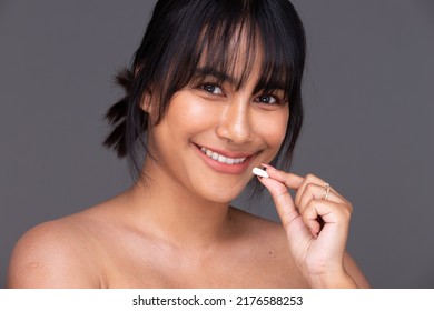 Asian Indian woman show beautiful smile happy lips, hold empty blank package capsule for treatment skin care. India Female feel wellbeing with medicine capsule in studio over gray background isolated