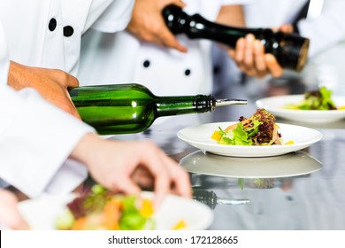 Asian Indonesian Chef Along With Other Cooks In Restaurant Or Hotel Commercial Kitchen Cooking, Finishing Dish Or Plate