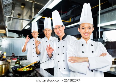 Asian Indonesian Chefs Along With Other Cooks In Restaurant Or Hotel Kitchen Cooking Or Fry With A Pan At The Stove