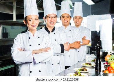 Asian Indonesian And Chinese Chefs Along With Other Cooks In Restaurant Or Hotel Commercial Kitchen Cooking, Finishing Dish Or Plate