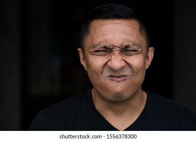 An Asian Indonesian guy twisted his face in agony. It looks like he is in pain. He closed both of his eyes and his mouth This portrait is taken with black background