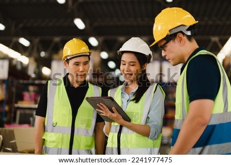 Asian Industrial Engineers talk with warehouse industrial workers using laptops to explain the procedure. They Work at the Heavy Industry Manufacturing Facility and industrial environments.