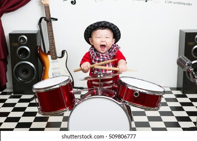 Asian Infant Playing Drum In Studio.