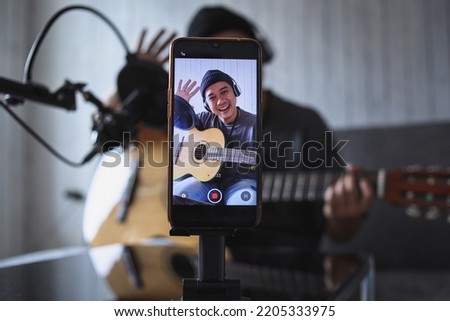 Asian influencer playing guitar during podcast or live video broadcast for the audience from the mobile phone at home