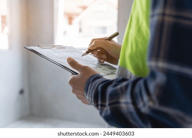 Asian inspector checking structure of new property and taking note in the clipboard for review and fix the house before sell to client