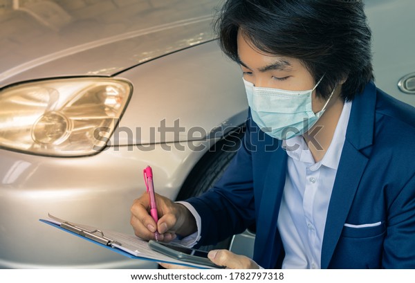 Asian Insurance Agent\
or Insurance Agency in Suit Wear Mask Writing Car Crash Report and\
Inspecting Car from Accident for Claim at Outdoor Place in Zoom\
View in Vintage Tone