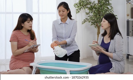asian japanese expectant mom in blue dress taking parenting class with her friend and asking questions to nurse.