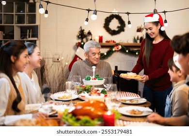 Asian joyful family gathering at Christmas, featuring a festive dinner, decorations, and a woman serving food to an elderly man in a cozy atmosphere - Powered by Shutterstock