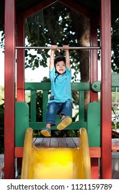 The Asian Kid 4 Year Old Wearing Helmet And Using Two Hand Holding Monkey Bar To Lift Up In The Air. The Asia Boy Play In The Playground. Concept Of Kids Activity And Safety Exercise , Play Time