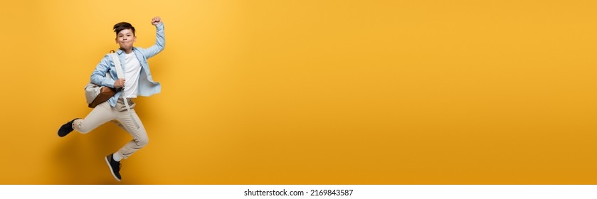Asian kid with backpack showing yes gesture and jumping on yellow background, banner