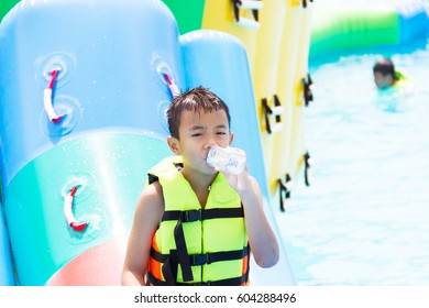 Asian Kid Drinking Water Inside Water Park.