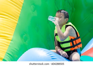 Asian Kid Drinking Water Inside Water Park.