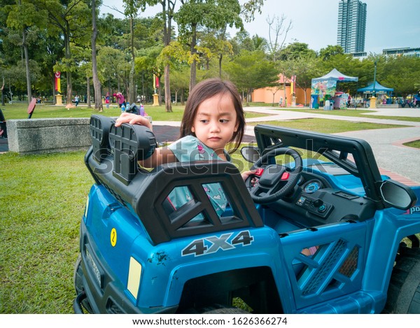 An\
Asian kid driving electric toy car in a tropical park. Outdoor\
toys. Children in battery power vehicle. Little girl riding toy\
truck in the garden. Family playing in the\
backyard.