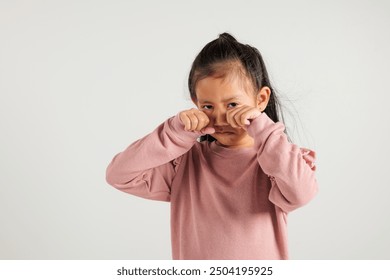 Asian kid girl emotional turmoil unfolds as cries and wipes tears away with fingers. Isolated on white background, kindergarten child expressive face paints vivid picture of sadness and frustration
