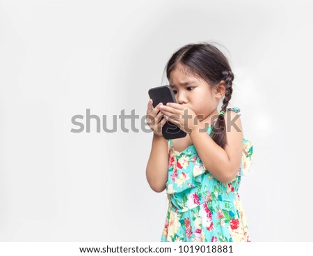 asian kid girl move mobile close face to watch video clip on isolate background in addict digital life style concept