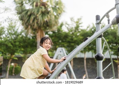 Asian Kid Girl Playing On A Swing And Having Fun In Park.Little Asian Girl Climbing Rope At Playground.Asian Child Girl Playing On Playground In Outdoor Park.Happy Little Asian Girl Outdoor Play Park.