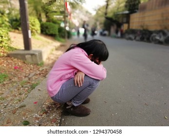 Asian Kid Girl Who Feel Bored Sitting And Hugging Their Knees On The Floor While Waiting Her Parent Shopping On Road. 
