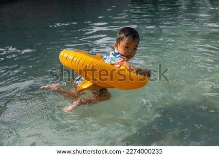 An Asian kid happy and enjoying playing water on pool with Kids' inflatable swim ring