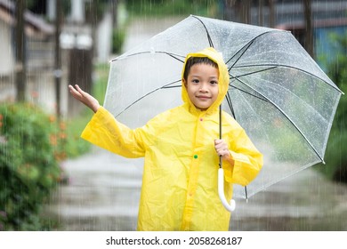 Asian Kid Holding An Umbrella And Catching Raindrops. Happy Asian Little Child Boy Having Fun Playing With The Rain In The Evening Sunlight.