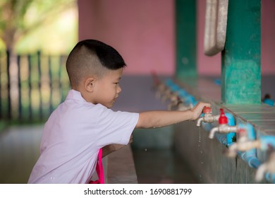 An Asian Kid Male Student Wears A School Uniform. He Is Reaching Out For The Tap After The Use. Kid Age 5-6 Years Old.