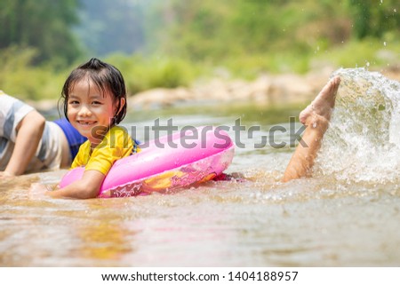 Asian kid with pink pool ring lying down on the riverside, Foot kicking water