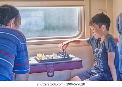 Asian Kid Playing Chess With His Grandfather At Train.