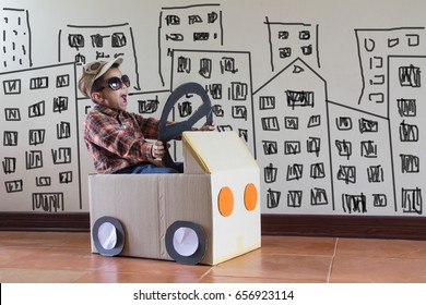 Asian kid playing with craft paper box like a car with city draw on the concrete wall