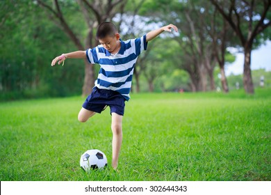 Asian Kid Playing Soccer In The Park, Authentic Action Kicking Ball