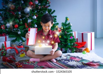 Asian Kid Sat In Front Of The Christmas Tree And Show A Wonderful Gift Box, It's Christmas Time