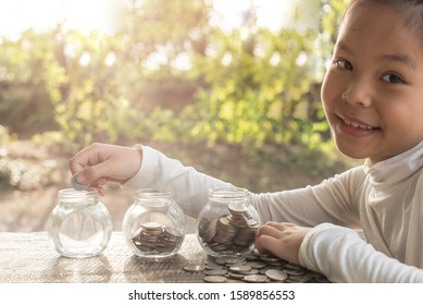 Asian Kid Saving Money Putting Coins Into Glass Bank, Hand Of Little Girl Putting Coins In Jar With Money Stack Step Growing Growth Saving Money, Concept Finance Business Investment, Money Saving