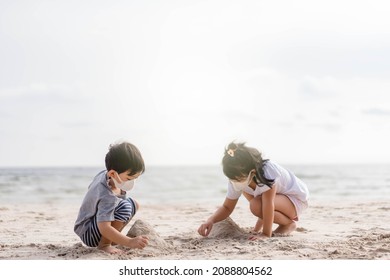 Asian kid sibling with mask playing on sand beach outdoor summer holidays.Children play sand castle. environment nature.Child development.vacation beach traveller child sister brother.Health medical .