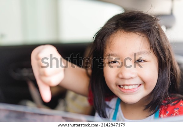 Asian kid tween girl thumb down with smile on\
seat.Family Riding Car Traveling Automobile. Asian family parenting\
and children with funny face.Angry selfish child.Sibling\
kid.spoiled child.bad\
feel.