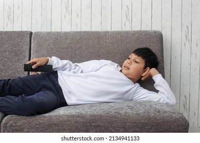Asian kid in white sweater laying down on the sofa and watching television
