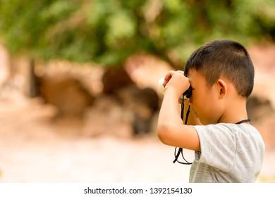 Asian Kids Boy Playing And Looking On Telescope In Zoo Park Nature, Blurred Nature Background, Kid Child Smiling For Watching, Wearing Gray Shirt In Journey Outdoor On Summer Holiday