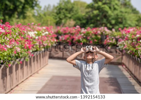 Asian kids boy playing and looking on telescope in park nature, blurred flower walking in nature background, kid child smiling for watching, wearing gray shirt in journey outdoor on summer holiday